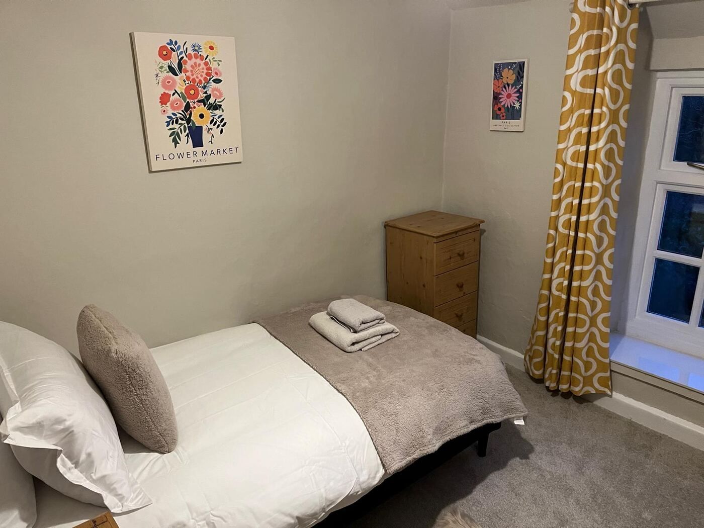 Single bedroom with bright flower prints and yellow curtains